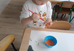 dziewczynka maluje dłoń pomarańczową farbą