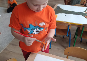 chłopiec maluje dłoń pomarańczową farbą