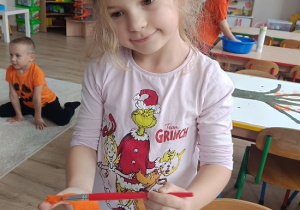 dziewczynka maluje dłoń pomarańczową farbą