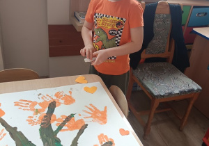 chłopiec maluje dłoń pomarańczową farbą