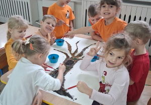 grupa dzieci maluje drzewo