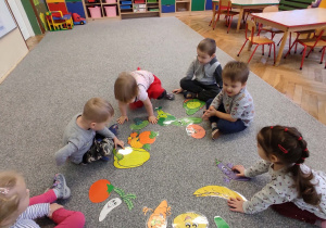 dzieci na dywanie oglądają warzywa z papieru