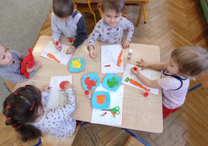 dzieci wykonują pracę plastyczna przy stoliku