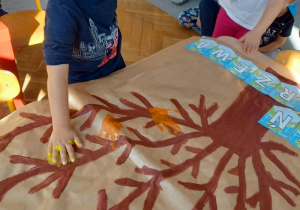 chłopiec odbija dłoń zamoczoną w farbie na szablonie drzewa
