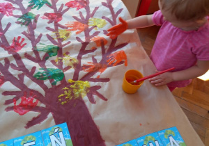 dziewczynka odbija dłoń zamoczoną w farbie na szablonie drzewa