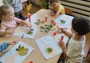 Dzieci wykonują pracę plastyczną przy stolikach.