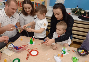 rodzice wspólnie z dziećmi ozdabiają styropianowe choinki