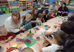 rodzice wspólnie z dziećmi ozdabiają styropianowe choinki