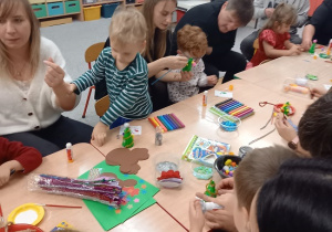 rodzice wspólnie z dziećmi ozdabiają styropianowe choinki