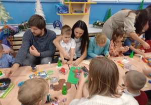 rodzice wspólnie z dziećmi ozdabiają styropianowe choinki