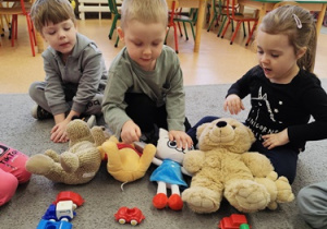 Dzieci siedzą na dywanie z zabawkami.