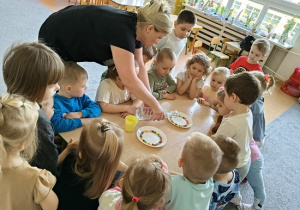dzieci wspólnie z nauczycielką wykonują eksperyment ze skitelsami