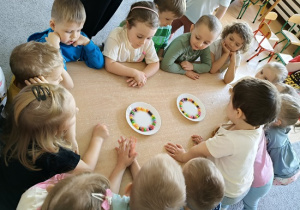 dzieci wspólnie z nauczycielką wykonują eksperyment ze skitelsami