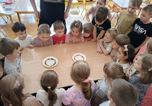 dzieci wspólnie z nauczycielką wykonują eksperyment ze skitelsami