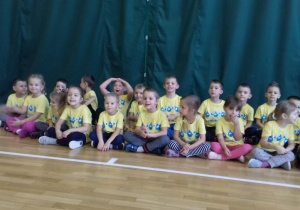 dzieci w żółtych koszulkach siedzą na hali w gromadce