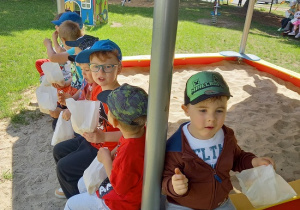 dzieci siedzą na piaskownicy i jedzą popcorn