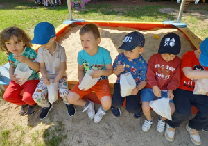 dzieci siedzą na piaskownicy i jedzą popcorn