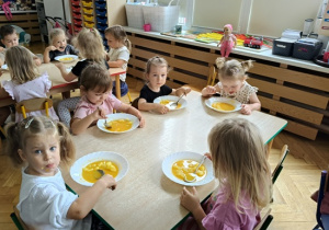 dzieci siedzą przy stoliku i jedzą zupę