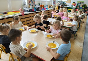 dzieci siedzą przy stoliku i jedzą zupę