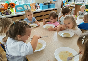 dzieci siedzą przy stoliku i jedzą zupę