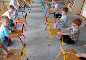 dzieci siedzą przed krzesełkami w szeregu
