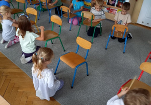 dzieci siedzą przed krzesełkami w szeregu