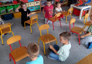 dzieci siedzą przed krzesełkami w szeregu