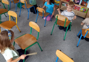 dzieci siedzą przed krzesełkami i stukają rytm