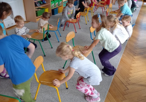 dzieci siedzą przed krzesełkami i wystukają rytm