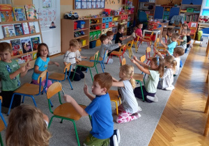 dzieci sedzą przed krzesełkami i wystukują rytm patyczkami