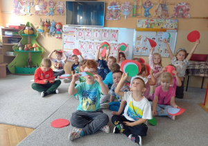 dzieci siedzą w grupie i pokazują kolorowe kropki