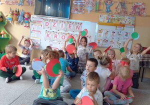 dzieci siedzą w grupie i pokazują kolorowe kropki
