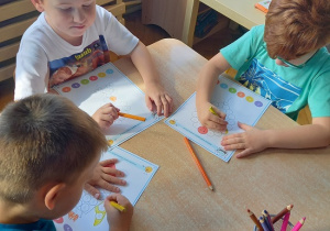 dzieci siedzą przy stoliku i wykonują kartę pracy