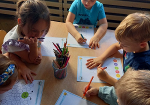 dzieci siedzą przy stoliku i wykonują kartę pracy