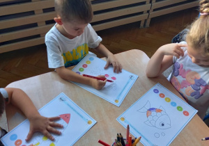dzieci siedzą przy stoliku i wykonują kartę pracy