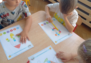 dzieci siedzą przy stoliku i wykonują kartę pracy