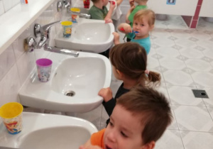 dzieci stoją przy umywalkach i szczotkują zęby