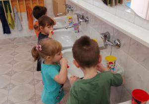 dzieci stoją przy umywalkach i szczotkują zęby