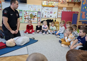 Pan strażak objaśnia dzieciom udzielanie pierwszej pomocy na fantomie