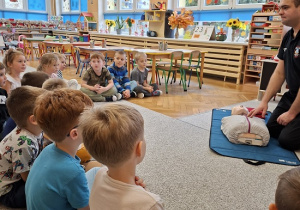 Pan strażak objaśnia dzieciom udzielanie pierwszej pomocy na fantomie