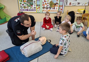 Pan strażak objaśnia dzieciom udzielanie pierwszej pomocy na fantomie