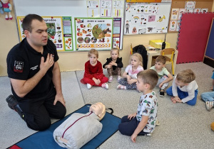 Pan strażak objaśnia dzieciom udzielanie pierwszej pomocy na fantomie