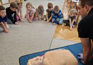 Pan strażak objaśnia dzieciom udzielanie pierwszej pomocy na fantomie