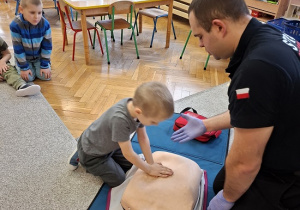 Pan strażak objaśnia dzieciom udzielanie pierwszej pomocy na fantomie