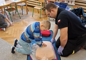 Pan strażak objaśnia dzieciom udzielanie pierwszej pomocy na fantomie