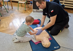 Pan strażak objaśnia dzieciom udzielanie pierwszej pomocy na fantomie