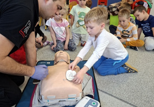 Pan strażak objaśnia dzieciom udzielanie pierwszej pomocy na fantomie