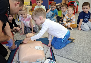 Pan strażak objaśnia dzieciom udzielanie pierwszej pomocy na fantomie