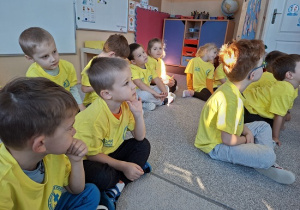 dzieci siedzą i słuchają w żółtych koszulkach