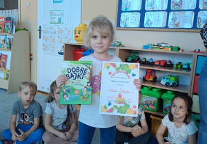 dziewczynka pozuje do zdjęcia z dyplomem i książką